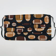 Load image into Gallery viewer, Made with three layers of footballs on black print 100% quilting cotton, this mask includes a filter pocket located in the pleats in the back of the mask for a filter of your choice, adjustable elastic ear loops and a bendable aluminum nose. Machine wash and dry after each use. 7” H x 7.5” W