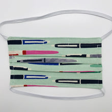 Load image into Gallery viewer, Made with three layers green, grey and pink pens on green print 100% quilting cotton, this mask includes a filter pocket located in the pleats in the back of the mask for a filter of your choice, over the head elastic loops and a bendable aluminum nose. Machine wash and dry after each use. 7” H x 7.5” W
