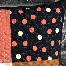 Load image into Gallery viewer, Scrappy Halloween pillow cover, 100% cotton in orange, black and gold prints. The pillow is quilted with a meandering design by machine with 40 wt Aurifil thread and has a hidden zipper in the back made of black Kona Cotton. The pillow cover only is offered and does not include the pillow form insert. The pillow insert needed is 18 x 18 inches. Machine wash with like colors in cold water with low suds soap such as Woolite, line dry.