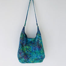 Load image into Gallery viewer, This beautiful 100% green, blue and purple leaves cotton batik makes a great slouch bag that is light and durable. The lining is beautiful Essex cotton\linen from Robert Kaufman and has a magnetic snap and inner pocket. 15.5” W & 14”H. Total length with strap 33”