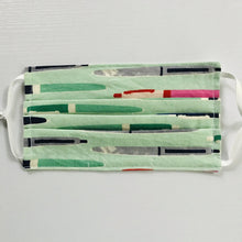 Load image into Gallery viewer, Made with three layers green, grey and pink pens on green print 100% quilting cotton, this mask includes a filter pocket located in the pleats in the back of the mask for a filter of your choice, adjustable elastic ear loops and a bendable aluminum nose. Machine wash and dry after each use. 7” H x 7.5” W
