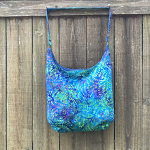 Load image into Gallery viewer, This beautiful 100% green, blue and purple cotton batik makesa great slouch bag that is light and durable. The lining is beautiful Essex cotton\linen from Robert Kaufman and has a magnetic snap and inner pocket. 15.5” W & 14”H. Total length with strap 33”