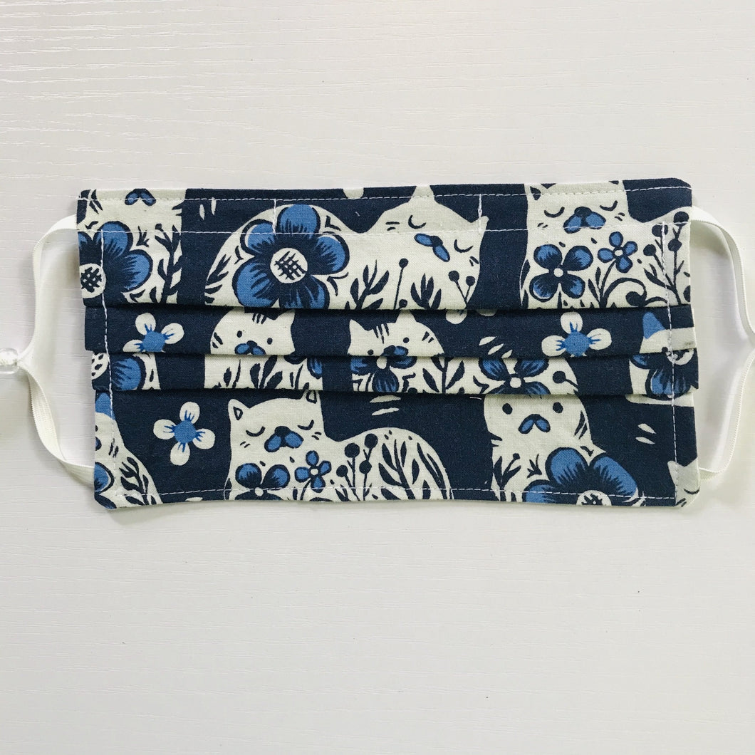 Made with three white cat designs on blue print 100% quilting cotton, this mask includes a filter pocket located in the pleats in the back of the mask for a filter of your choice, adjustable elastic ear loops and a bendable aluminum nose. Machine wash and dry after each use. 7” H x 7.5” W