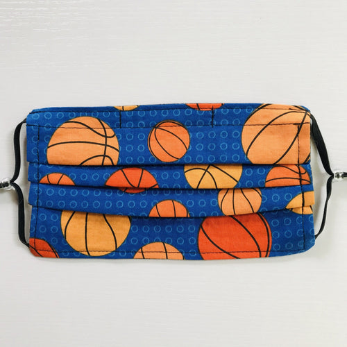 100% quilting-weight sports themed print cotton fabric face mask with adjustable elastic ear loops and bendable nose piece. Washable, reusable fabric face mask. Wash in washing machine and dry in dryer after each use. 7” H x 7.5” W  These tossed basketballs on blue are from the fabric Collection: Sports Life by Robert Kaufman Fabrics