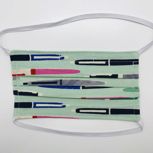100% cotton novelty aqua green print face mask with elastic bands and bendable nose piece. Washable, reusable fabric face mask. Wash in washing machine and dry in dryer after each use. Fabric Collection - Cotton + Steel - Trinket Pens Aqua 7” H x 7.5” W