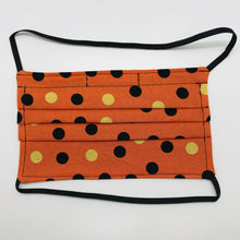 Load image into Gallery viewer, Made with three layers of orange and gold dots on black print 100% quilting cotton, this mask includes a filter pocket located in the pleats in the back of the mask for a filter of your choice, over the head elastic loops and a bendable aluminum nose. Machine wash and dry after each use. 7” H x 7.5” W
