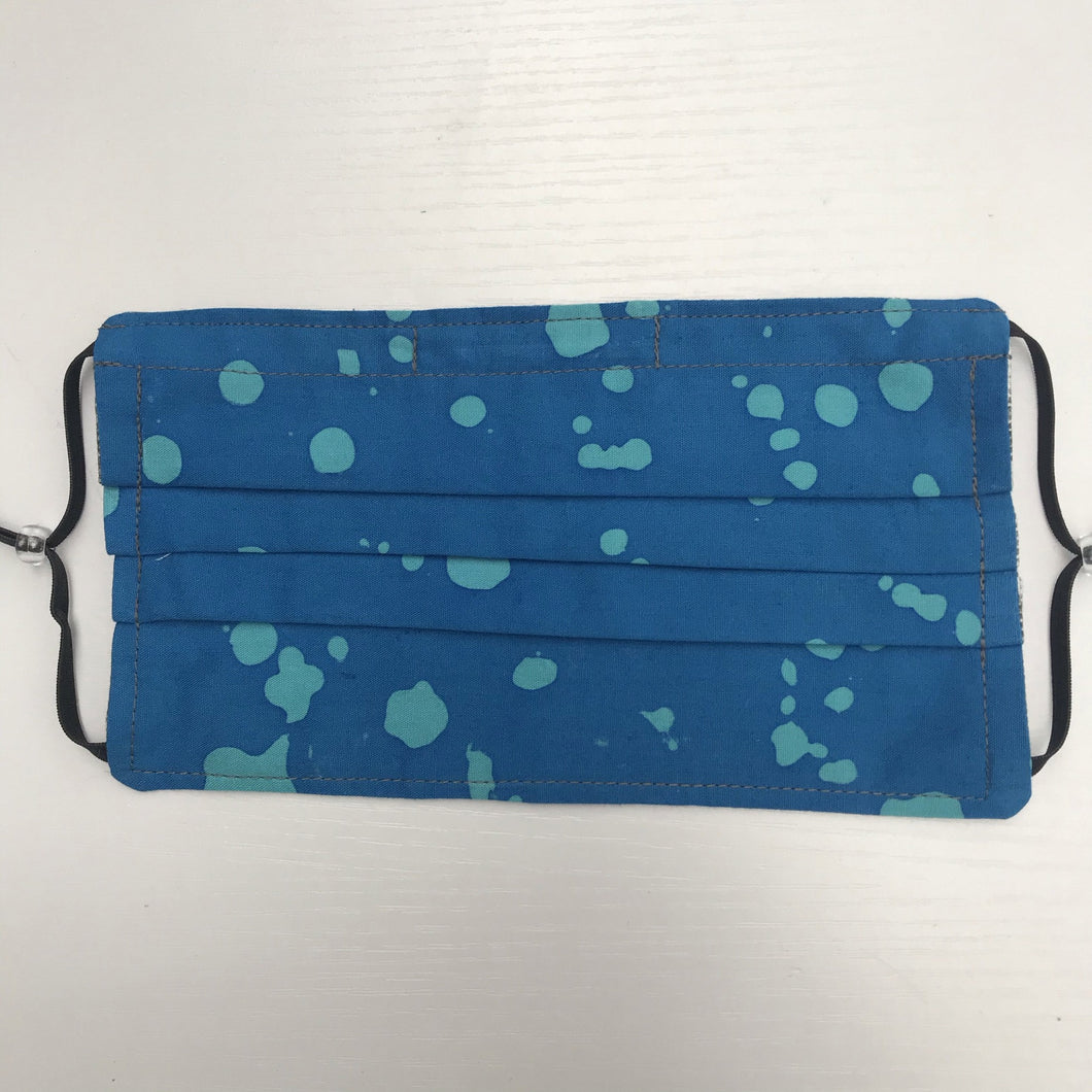 100% quilting-weight batik cotton blue splatter design face mask with adjustable elastic ear loops and bendable nose piece. Washable, reusable fabric face mask. Wash in washing machine and dry in dryer after each use. 7” H x 7.5” W  Fabric from the Handcrafted Batiks collection by Alison Glass from Andover Fabrics. 