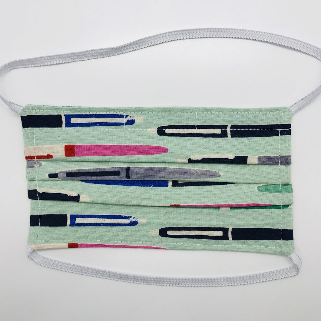 100% cotton novelty aqua green print face mask with elastic bands and bendable nose piece. Washable, reusable fabric face mask. Wash in washing machine and dry in dryer after each use. Fabric Collection - Cotton + Steel - Trinket Pens Aqua 7” H x 7.5” W