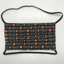 Load image into Gallery viewer, Made with three layers of trick or treat words and orange pumpkins on black print 100% quilting cotton, this mask includes a filter pocket located in the pleats in the back of the mask for a filter of your choice, over the head elastic loops and a bendable aluminum nose. Machine wash and dry after each use. 7” H x 7.5” W
